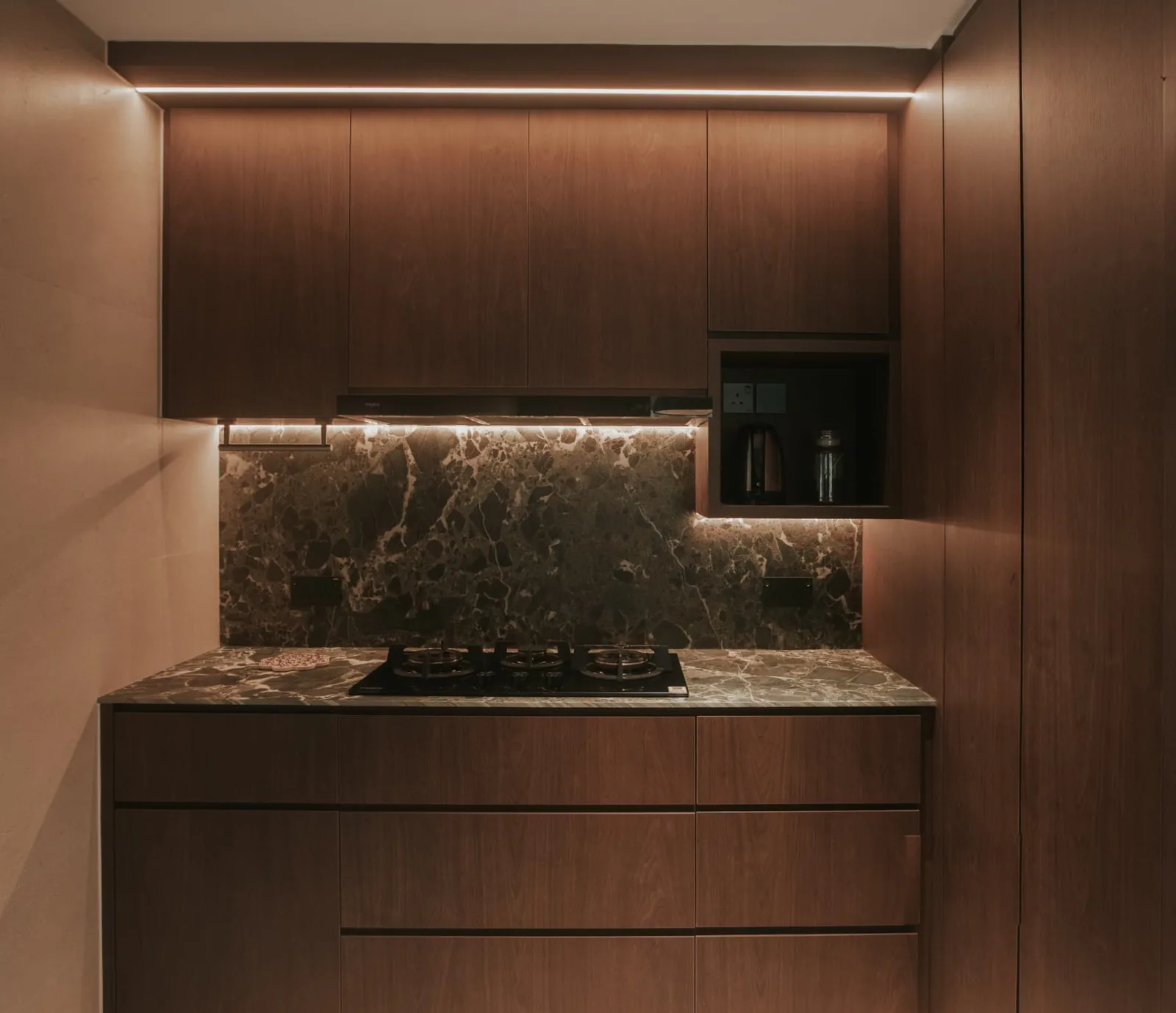 Kitchen with a warm linear light washing the ceiling above the upper cabinets and under-cabinet task lighting across the stone backsplash