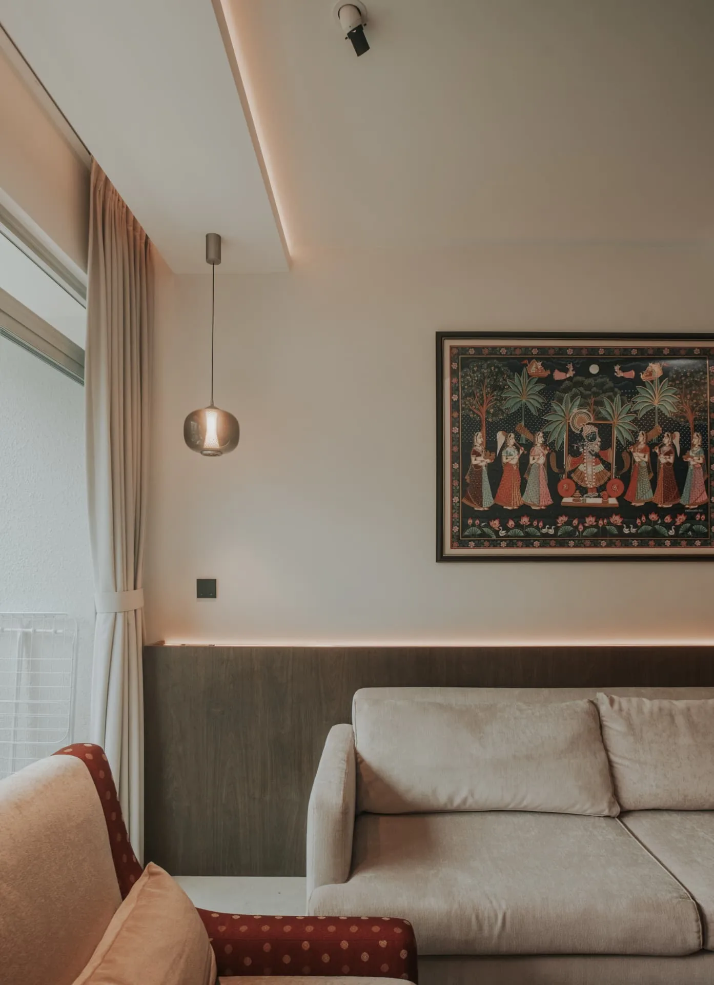 Living room with a glass pendant, framed artwork and a warm cove light above timber panelling