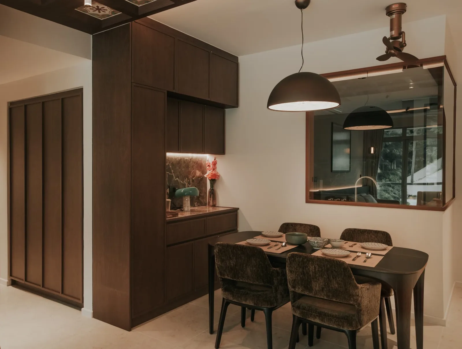 Warmly lit residential dining area with a wide pendant over the table and integrated lighting in the adjoining kitchen